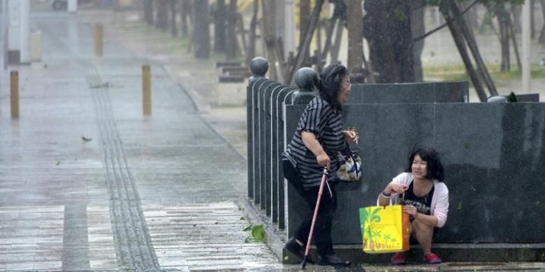 Ilustrasi : Dua perempuan warga kota Naha, Okinawa, Jepang berlindung dari terjangan badai