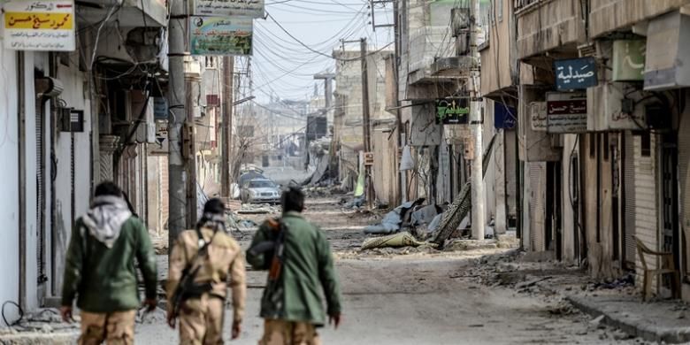 Beberapa pejuang Kurdi Suriah berjalan di salah satu sudut kota Kobani yang hancur lebur akibat pertempuran. Setelah empat bulan pertumpahan darah yang brutal, pejuang Kurdi yang dibantu serangan udara koalisi internasional berhasil memukul mundur pasukan ISIS.