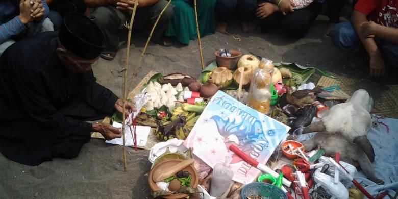 Seorang tokoh masyarakat mendoakan kepala kerbau dan berbagai jenis makanan yang akan dilarung ke laut dalam upacara sedekah laut untuk mengucapkan syukur kepada Tuhan atas rezeki yang melimpah.