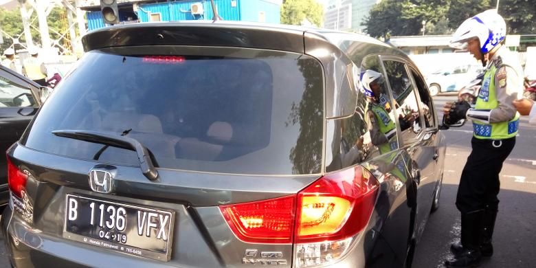Petugas kepolisian saat menegur pengendara mobil yang berpelat nomor genap di lampu merah Bundaran Senayan pada Senin (27/6/2016). Hari ini merupakan masa uji coba penerapan ganjil genap disejumpah ruas jalan di Jakarta. 