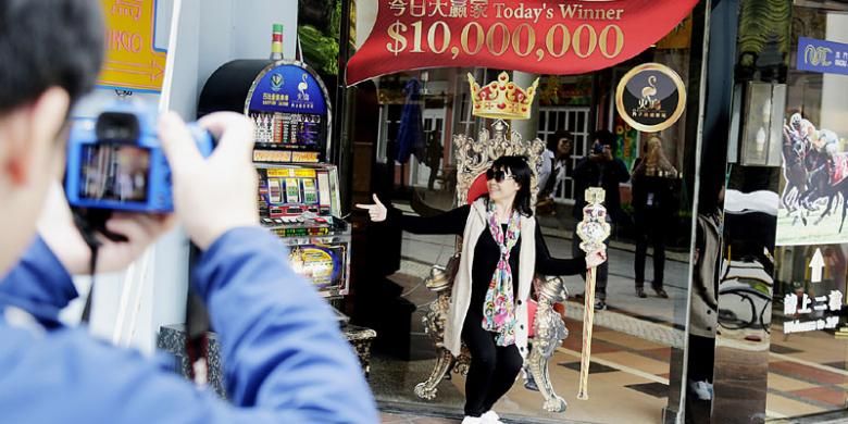 Seorang wisatawan dari Korea Selatan berfoto di sebuah dinding berstiker foto kursi dan tongkat raja di belakang sebuah kasino di Makau.
