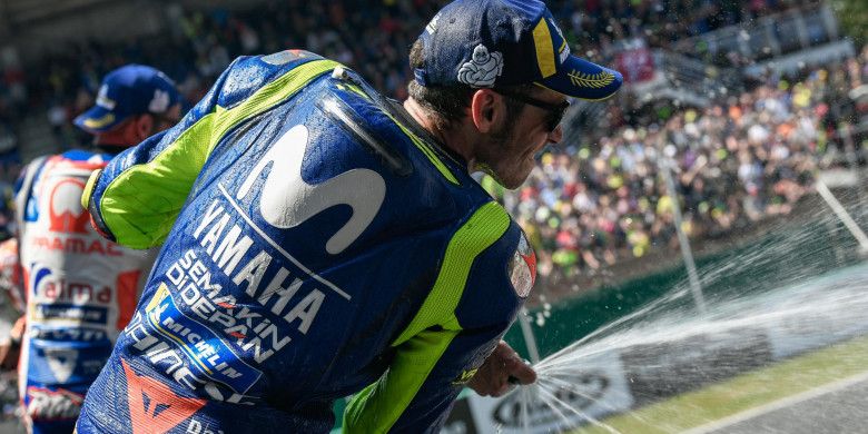 Pebalap Movistar Yamaha, Valentino Rossi, menyemburkan isi sampanye saat merayakan keberhasilannya finis di posisi ketiga pada balapan seri kelima MotoGP Prancis di Sirkuit Le Mans, Minggu (20/5/2018).