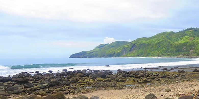 Panorama kawasan pantai nelayan di Menganti dengan tebing perbukitan hijau yang menjorok ke lautan.