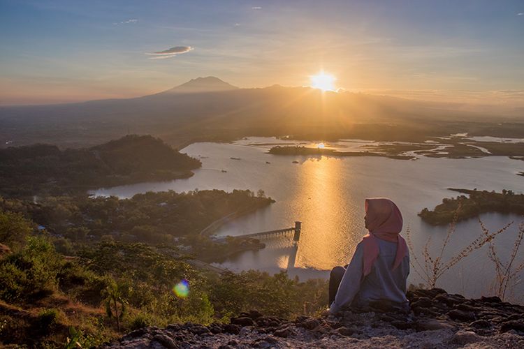 Seorang pengunjung berfoto dengan latar belakang keindahan matahari terbit di Watu Cenik, Wonogiri (13/06/2019).
