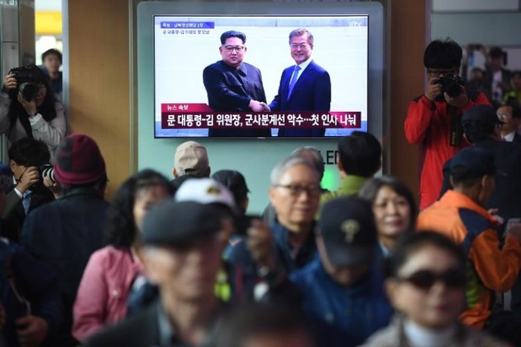 Masyarakat menyaksikan layar televisi yang memperlihatkan cuplikan langsung pertemuan Presiden Korea Selatan Moon Jae-in dan pemimpin Korea Utara Kim Jong Un, di sebuah stasiun kereta api di Seoul, Jumat (27/4/2018). (AFP/Jung Yeon-je)