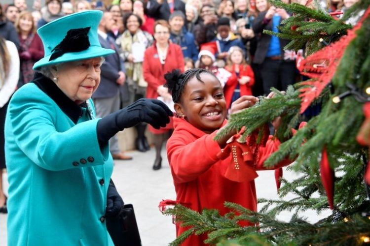 Ratu Elizabeth II dan Shylah Gordon menghias pohon natal. Ratu mengunjungi lembaga badan amal anak-anak Coram di London pada 5 Desember 2018. (AFP/TOBY MELVILLE)