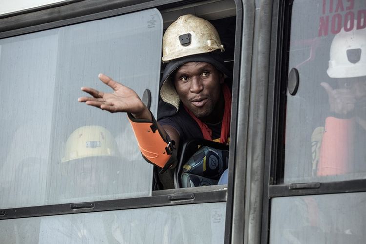 Salah seorang bekerja melambaikan tangan dari dalam bus, setelah keluar dengan selamat dari dalam tambang di Beatrix, Afrika Selatan.