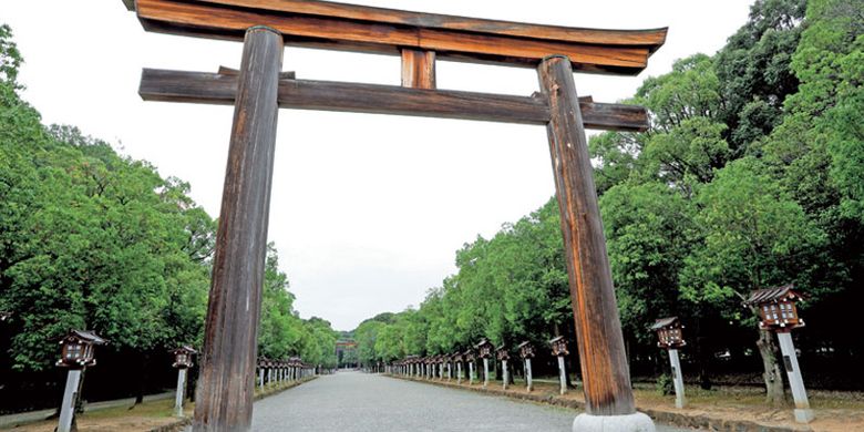 Gerbang kuil (tori) besar akan menyambut kita di jalan masuk Kuil Kashihara Jingu di kota Nara, Jepang. Pohon ek berjajar di kanan dan kiri jalan.