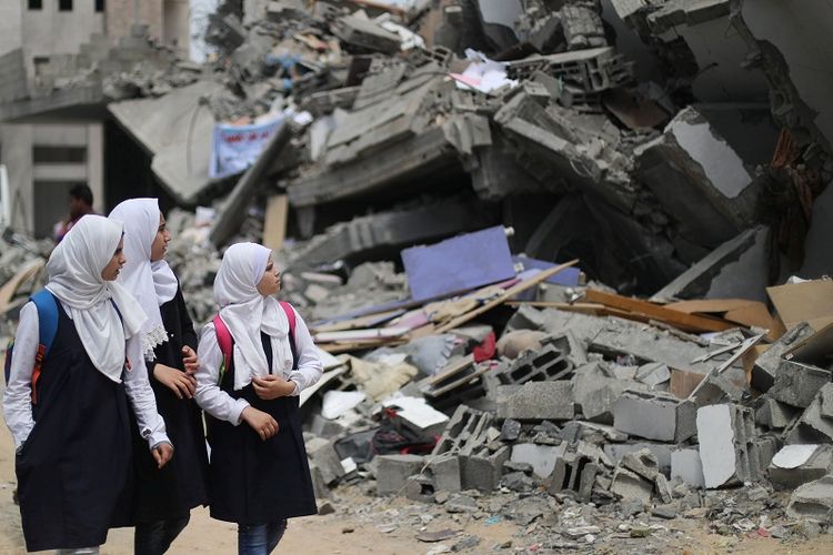 Pelajar Palestina di Gaza menyaksikan bangunan yang dihancurkan oleh serangan udara Israel di dekat sekolah mereka yang rusak, Selasa (7/5/2019). (REUTERS/Mohammed Salem)
