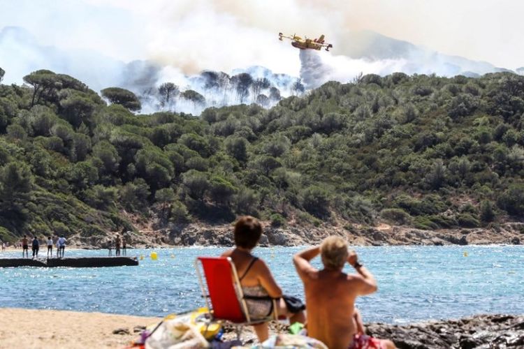 Turis di pantai La Croix-Valmer dekat Saint-Tropez, Perancis menyaksikan sebuah pesawat Canadair menjatuhkan air di atas hutan yang terbakar.