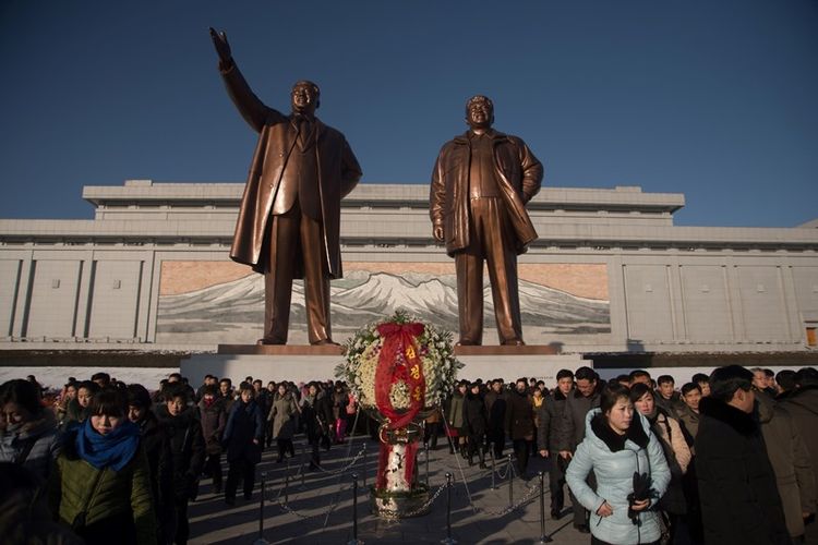 Orang-orang berjalan di depan patung pemimpin Korea Utara Kim Il Sung (kiri) dan Kim Jong Il (kanan), setelah meletakkan bunga untuk menandai ulang tahun keenam kematian Kim Jong Il, di bukit Mansu, Pyongyang, Minggu (17/11/2017). (AFP/Kim Won Jin)