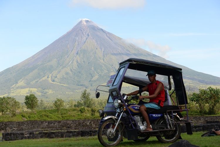 Foto ini diambil pada  11 Desember 2014 menunjukkan sepeda roda tiga bermotor yang melaju melewati gunung api Mayon di dekat kota Legazpi, provinsi Albay, Filipina. (AFP/Ted Aljibe)
