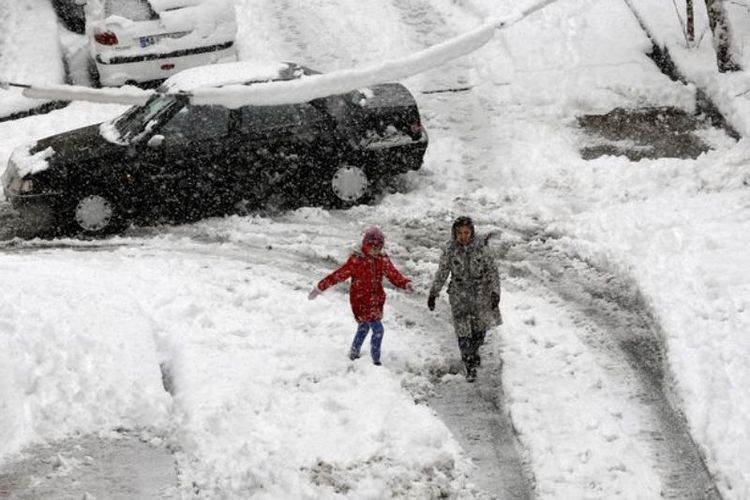 Dua anak di Teheran, Iran berjalan di antara salju yang bertumpuk di jalanan.