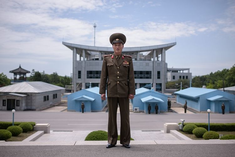 Dalam foto ini terlihat seorang prajurit Korea Utara berpose di Zona Demiliterisasi yang memisahkan kedua Korea. Di belakangnya terlihat Rumah Perdamaian lokasi KTT Korea yang akan digelar pada Jumat (27/4/2018).