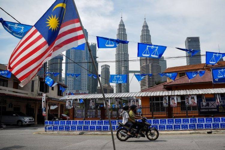 Bendera Malaysia berkibar dengan latar belakang pemandangan menara kembar Petronas dan bendera kecil dari partai Barisan Nasional. (AFP/Manan Vatsyayana)