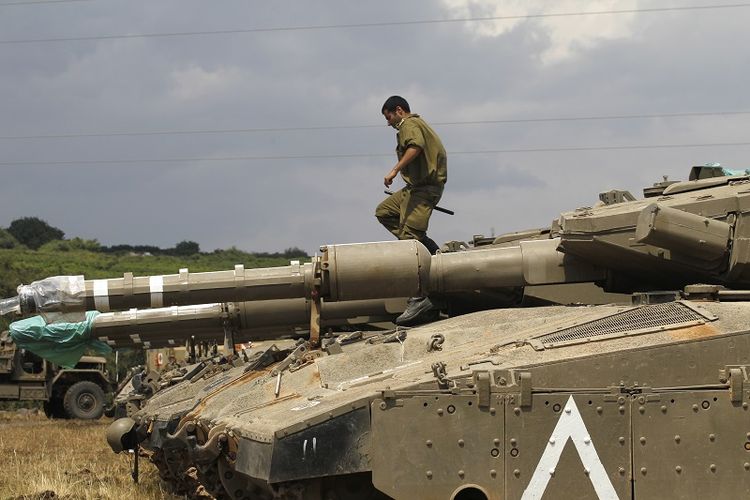 Seorang prajurit Israel tengah berdiri di atas tank Merkava IV yang disiagakan di Dataran Tinggi Golan yang berbatasan dengan Suriah.