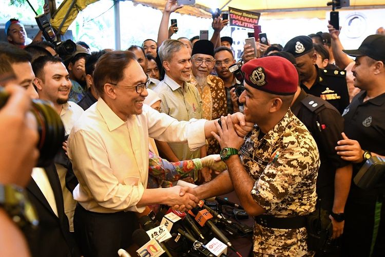 Mantan pemimpin oposisi Anwar Ibrahim (L) menjabat tangan seorang sipir penjara setelah memberikan keterangan pers di kediamannya pada Rabu (16/5/2018). 