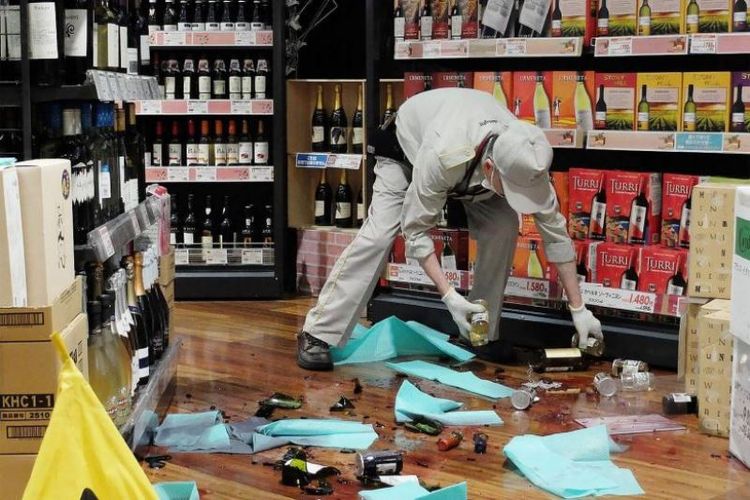 Seorang karyawan toko membersihkan botol-botolyang terjatuh dari rak akibat gempa di Osaka, Jepang, pada Senin (18/6/2018). (AFP/Jiji Press/STR)