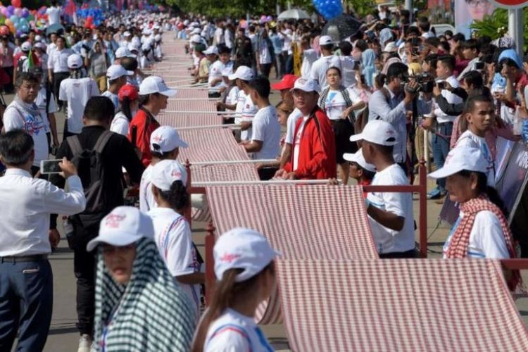 Warga Kamboja membentangkan syal krama sepanjang 1.149,8 meter untuk memecahkan rekor Guinness sebagai syal tenun terpanjang dunia. Acara ini digelar di Phonm Penh, Kamboja, Minggu (1/7/2018). (AFP/Tang Chhin)