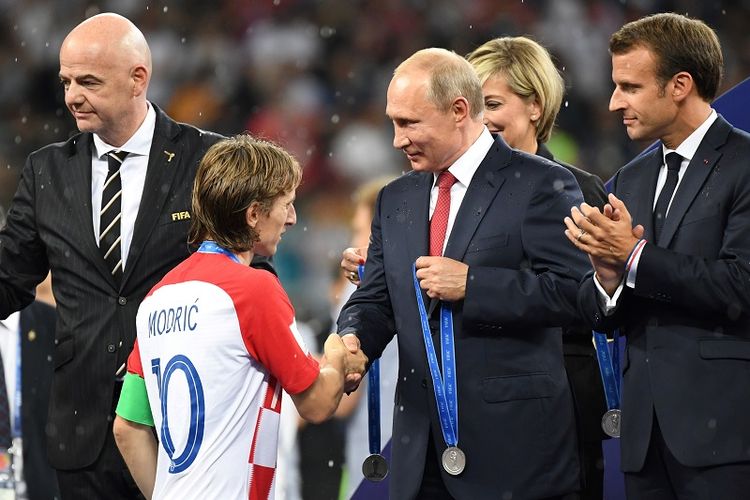 Presiden Rusia Vladimir Putin menjabat tangan kapten timnas Kroasia Luca Modric sesaat sebelum penyerahan medali usai laga final Piala Dunia 2018. Terlihat di podium, Presiden Perancis Emmanuel Macron.