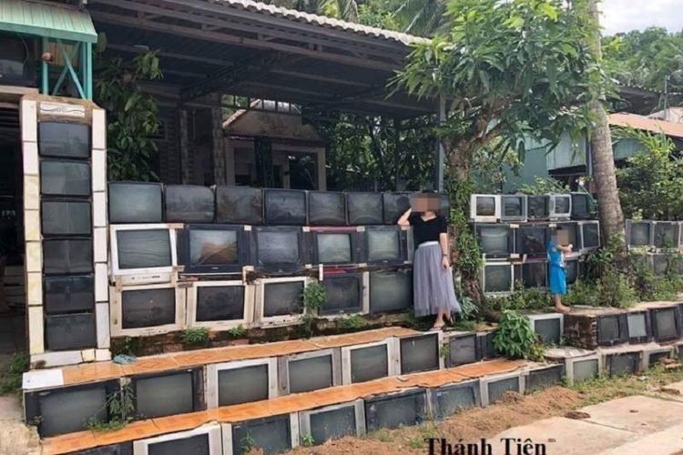 Dua orang pengunjung berfoto di depan sebuah rumah yang mendirikan pagar dari kumpulan televisi bekas di Hon Thom, Vietnam.