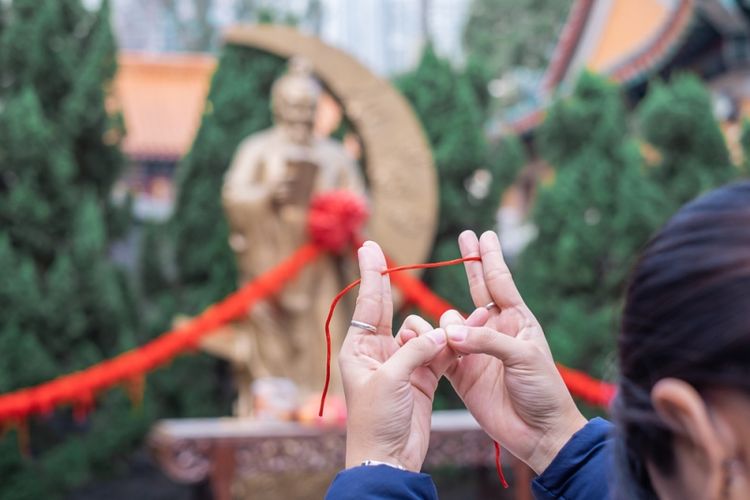 Seorang perempuan mengikat tali merah dan berdoa di depan patung Yue Lao atau Dewa Cinta di Kuil Wong Tai Sin, Hong Kong. (Shutterstock)