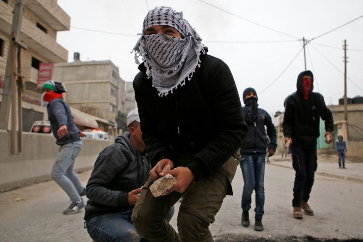 Seorang demonstran Palestina membawa batu ketika bentrok dengan aparat Israel di pos militer Qalandia