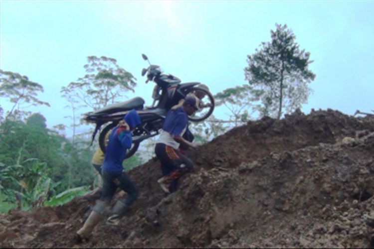 Sejumlah warga sekitar lokasi longsor yang menimbun jalur  utama penghubung antar kecamatan di Trenggalek Jawa Timur,memikul sepeda motor milik warga yang hendak menyebrang (03/02/2018)