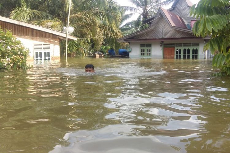 Seorang warga keluar dari rumahnya yang dilanda banjir di Desa Padang Luas, Kecamatan Tambang, Kabupaten Kampar, Riau, Jumat (14/12/2018)