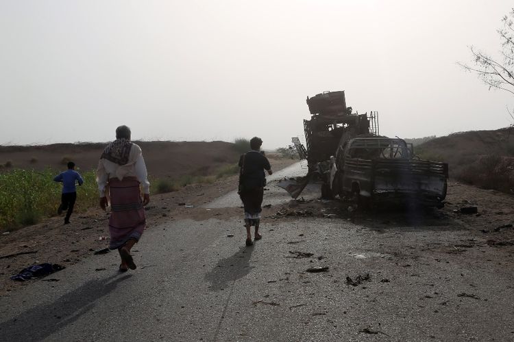 Warga Yemen melintas di dekat bangkai kendaraan yang hancur akibat pertempuran antara pasukan pemerintah dengan pemberontak Houthi di dekat Hodeidah.
