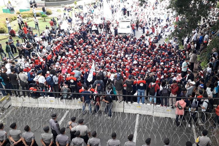 Massa peserta aksi Hari Buruh Internasional 2019 dari KSPN menggelar orasi di hadapan barikade kawat berduri di Jalan Medan Merdeka Barat, Rabu (1/5/2019).
