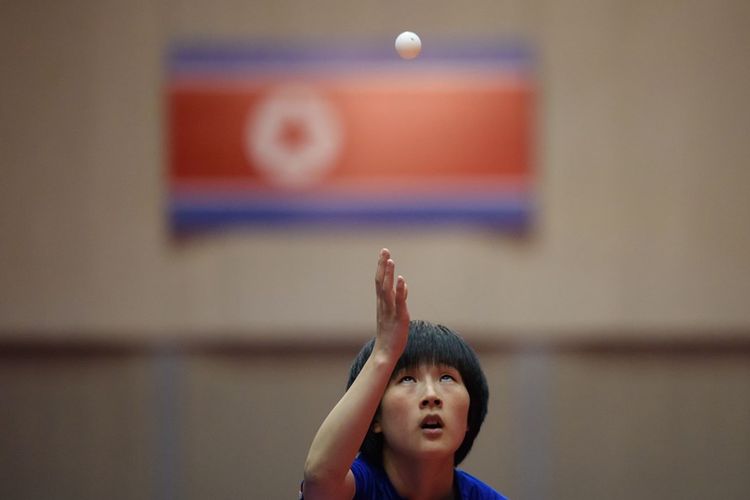 Atlet tenis meja Korea Utara bersiap melakukan servis dengan latar belakang bendera Korea Utara, saat mengikuti ajang kejuaraan tenis meja tahunan Pyongyang Open pada Juni 2018.