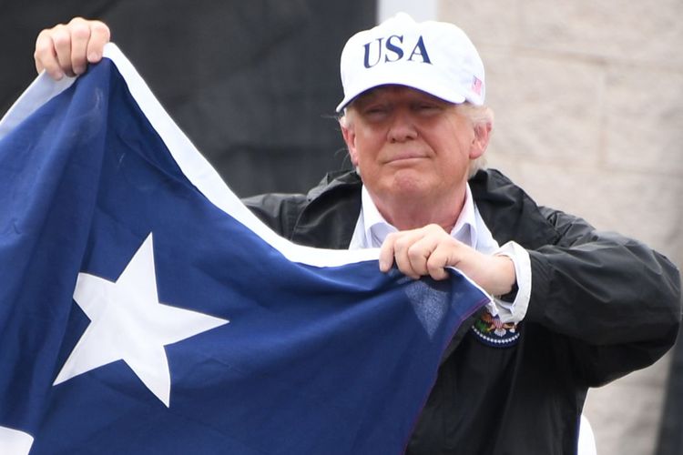Mengenakan jaket lengkap dengan topi berlabel USA, Trump terlihat mengangkat bendera negara bagian Texas, saat berkunjung ke wilayah terlanda badai Harvey, Selasa (29/8/2017)