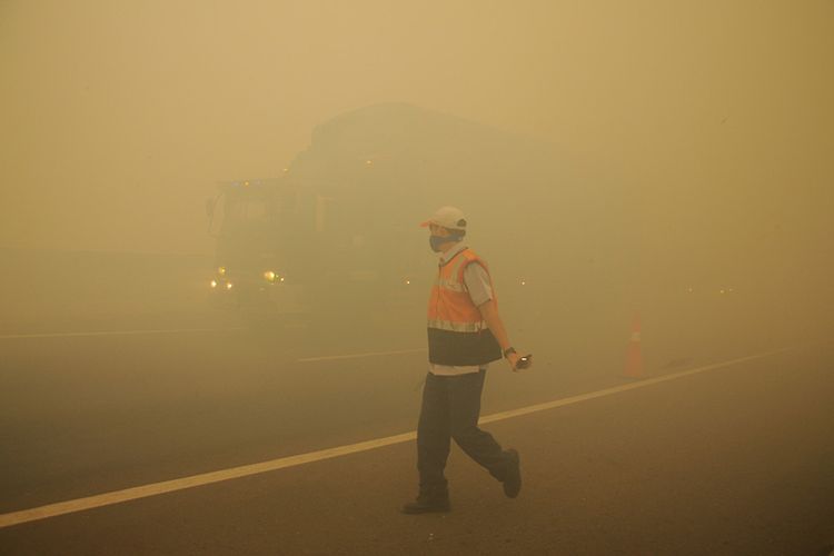 Petugas jalan tol Indralaya-Palembang melakukan pengaturan lalu lintas saat terjadi kabut asap akibat kebakaran lahan gambut di Desa Pulau Semembu, Indralaya Utara, Ogan Ilir, Sumatra Selatan, Senin (5/8/2019). BPBD Sumsel mencatat per awal Agustus, Ogan Ilir menjadi kabupaten dengan wilayah kebakaran lahan terluas yaitu seluas 121,5 hektare dari enam wilayah rawan kebakaran lahan dan hutan di Sumsel.