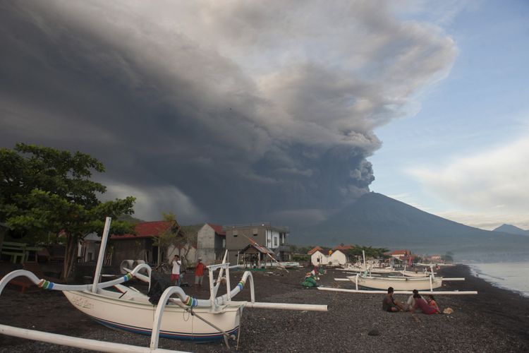 Sejumlah warga menikmati liburan dengan latar belakang Gunung Agung meletus, di Pantai Jemeluk, Karangasem, Bali, Minggu (26/11/2017). Pusat Vulkanologi dan Mitigasi Bencana Geologi menyatakan telah terjadi letusan freatik kedua pada pukul 17.20 Wita yang disusul dengan semburan asap dan abu vulkanis hingga ketinggian 3.000 meter. 