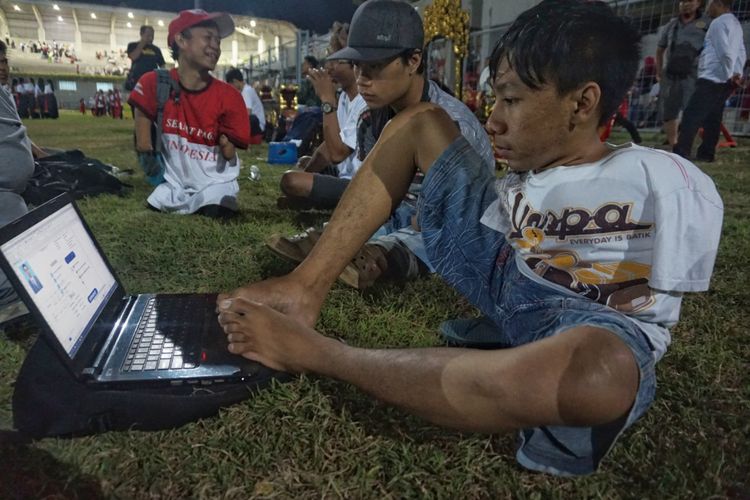 Wahyu Rianto sedang mengoperasikan laptop miliknya saat berkumpul dengan rekan-rekannya di Stadion Diponegoro Banyuwangi, Kamis (18/10/2018). 