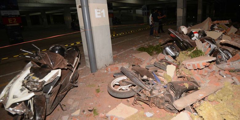 Warga melihat kendaraan yang hancur tertimpa puing bangunan yang runtuh akibat gempa, di salah satu mall, di Denpasar, Minggu (5/8/2018). Gempa yang mengguncang Lombok, Nusa Tenggara Barat, juga terasa hingga Bali.