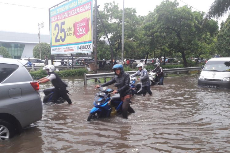 Pengendara motor menuntun sepeda motornya yang mogok akibat nekat melintasi Jalan Danau Sunter Utara yang terendam banjir, Selasa (27/3/2018).