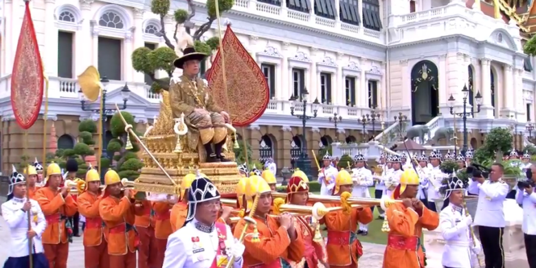 Raja Thailand Maha Vajiralongkorn duduk di atas tandu kerajaan berwarna emas yang diangkat oleh pasukan berseragam oranye dalam perjalanan menuju Kuil Emerald Buddha di Bangkok setelah dinobatkan pada Sabtu (4/5/2019).