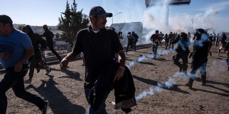 Para migran berlari menyelamatkan diri dari gas air mata yang ditembakkan polisi perbatasan Amerika Serikat-Meksiko Minggu (25/11/2018).