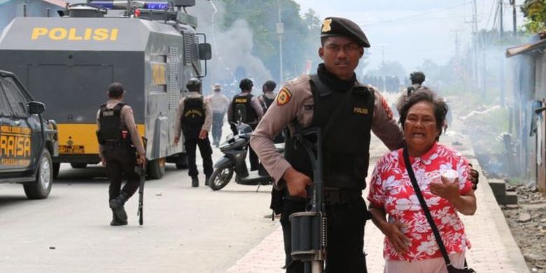 Petugas polisi mengantar seorang ibu menjauh dari pusat kerusuhan di Mimika, Papua Barat. 