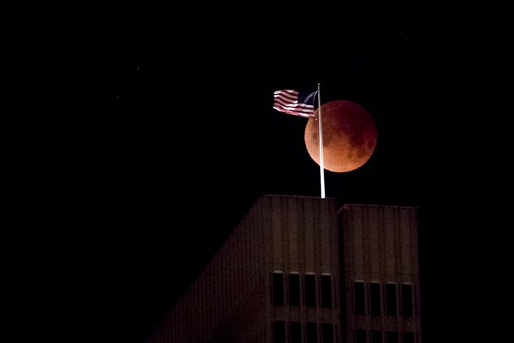 Penampakan bulan saat terjadinya gerhana bulan total atau super blue blood moon, di sela bendera AS, San Fransisco, California, Rabu (31/1/2018) malam. Warga di berbagai belahan dunia antusias menyaksikan fenomena langka yang terjadi bertepatan saat bulan berada dalam konfigurasi supermoon dan blue moon ini terjadi sekitar dalam kurun waktu 150 tahun sekali.