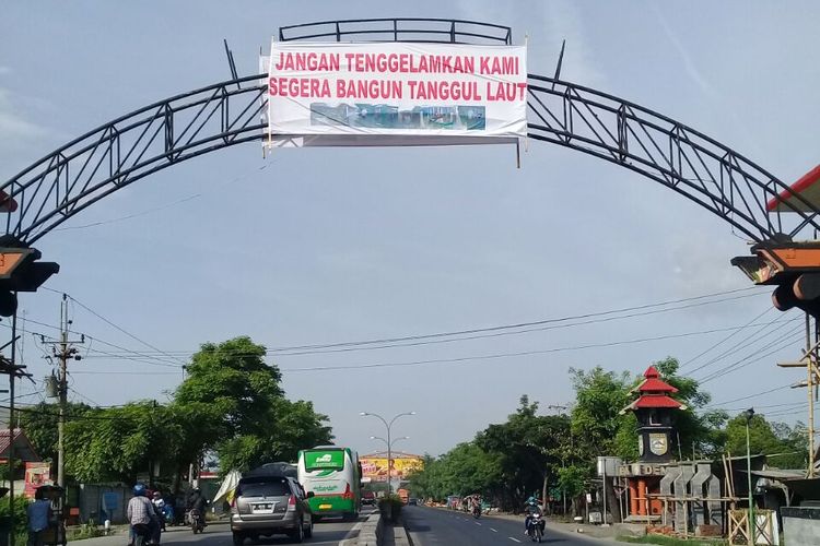 Spanduk bernada protes agar dibangun tanggul laut,  terpasang di gerbang masuk Demak, Minggu (5/12/2017) 