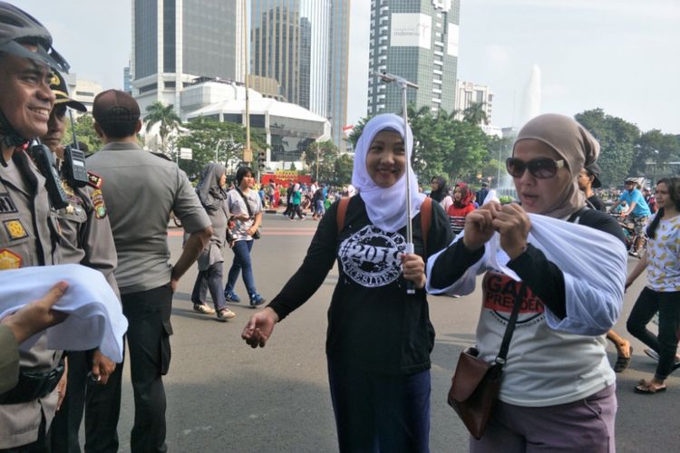 Satuan Polisi Pamong Praja (Satpol PP) DKI Jakarta membagikan kaus putih polos untuk warga yang mengenakan kaus dengan tanda pagar #2019GantiPresiden di kawasan Car Free Day (CFD) di Jalan Sudirman-Thamrin, Jakarta Pusat, Minggu (6/5/2018).