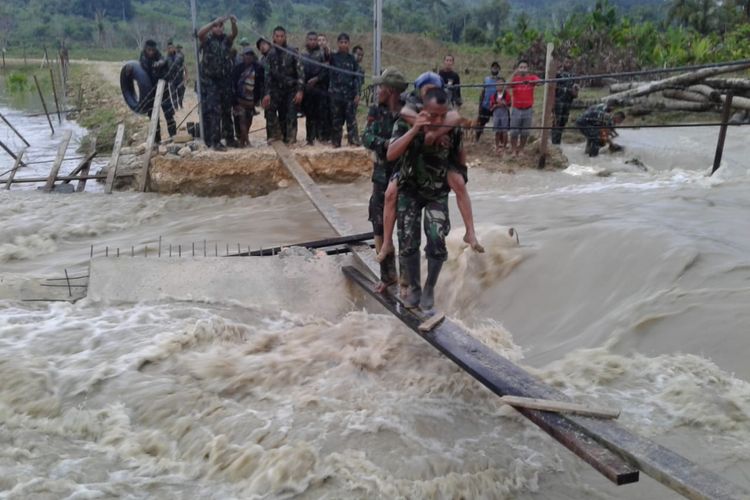 Prajurit TNI menggendong seorang lansia melintasi sungai untuk keluar dari lokasi banjir