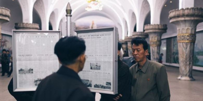 Beberapa ornag terlihat sedang membaca papan surat kabar di stasiun kereta Pyongyang Metro, Korea Utara. (Elaine Li via CNN)