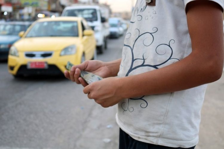 Seorang anak di Mosul, Irak, berjuang untuk mencari uang di jalanan dengan mengemis, menjual air mineral, dan tisu. Foto ini menunjukkan seorang anak memegang uang tunai di jalan pada Sabtu (7/7/2018). (AFP/Waleed Al-Khalid)