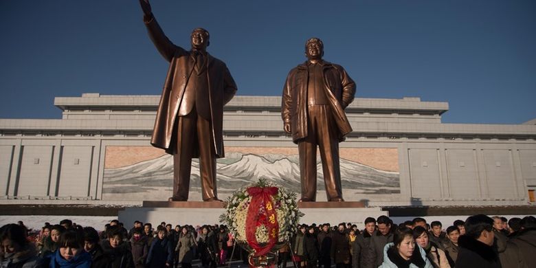 Orang-orang berjalan di depan patung pemimpin Korea Utara Kim Il Sung (kiri) dan Kim Jong Il (kanan), setelah meletakkan bunga untuk menandai ulang tahun keenam kematian Kim Jong Il, di bukit Mansu, Pyongyang, Minggu (17/11/2017). (AFP/Kim Won Jin)