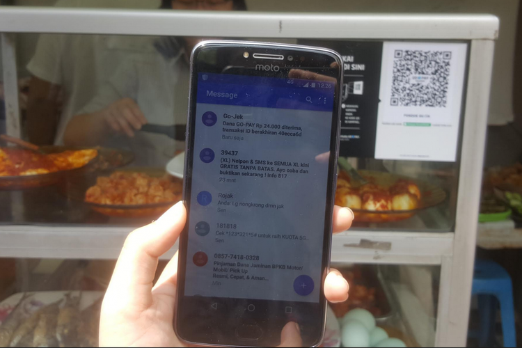 Penjual warung makanan pinggir jalan menerima pesan ketika pembeli berhasil membayar dengan Go-Pay.