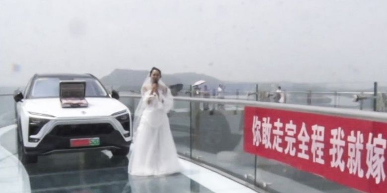 Dalam gambar terlihat seorang wanita berdiri di jembatan kaca dengan di belakangnya terdapat mobil dan uang. Wanita itu diputus setelah memaksa pacarnya untuk berjalan di jembatan tersebut.